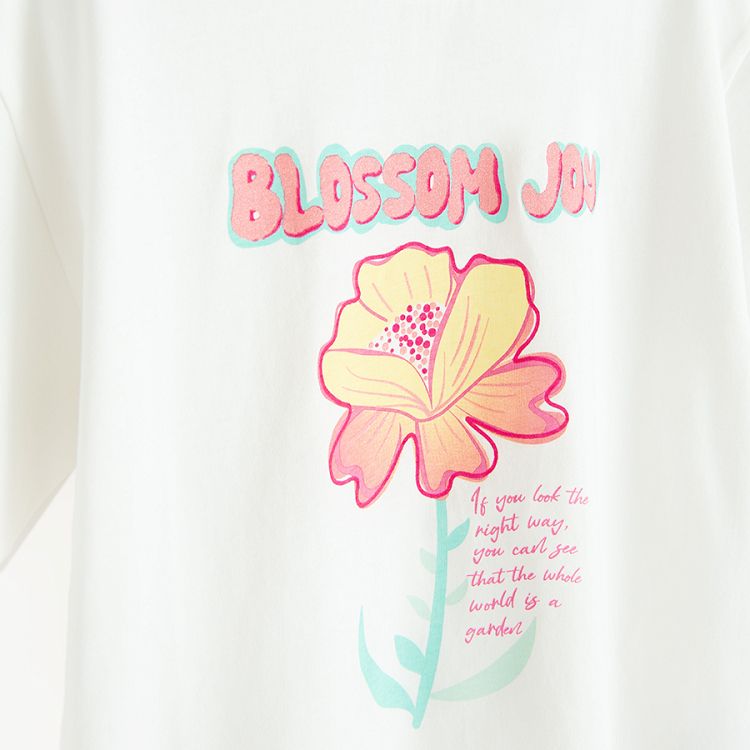 חולצת טריקו לבנה עם הדפס פרח וכיתוב 'Blossom Joy'